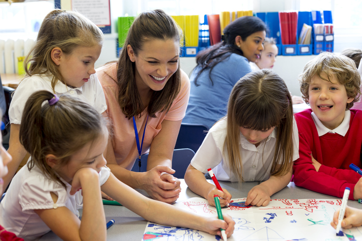 teacher sat with primary school learners smiling and teaching